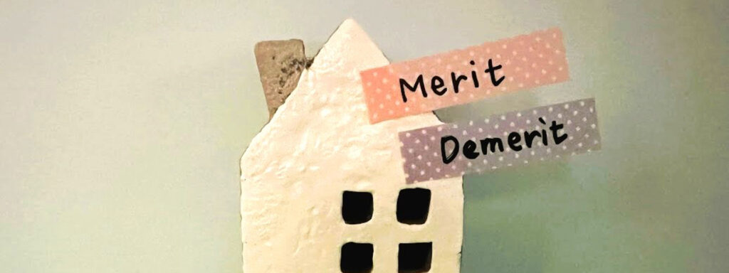 「Merit」と「Demerit」のテープが貼られた家の模型