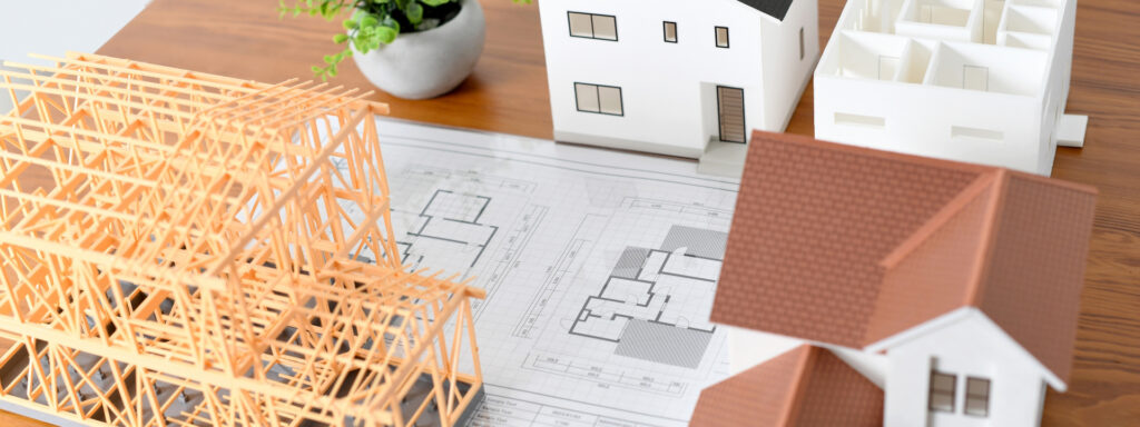 図面の上に置かれた住宅模型と木造フレーム